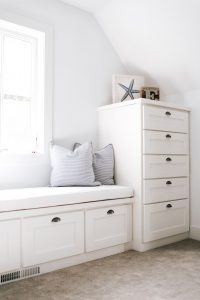 White shaker style bench under window with stack of drawers on the side